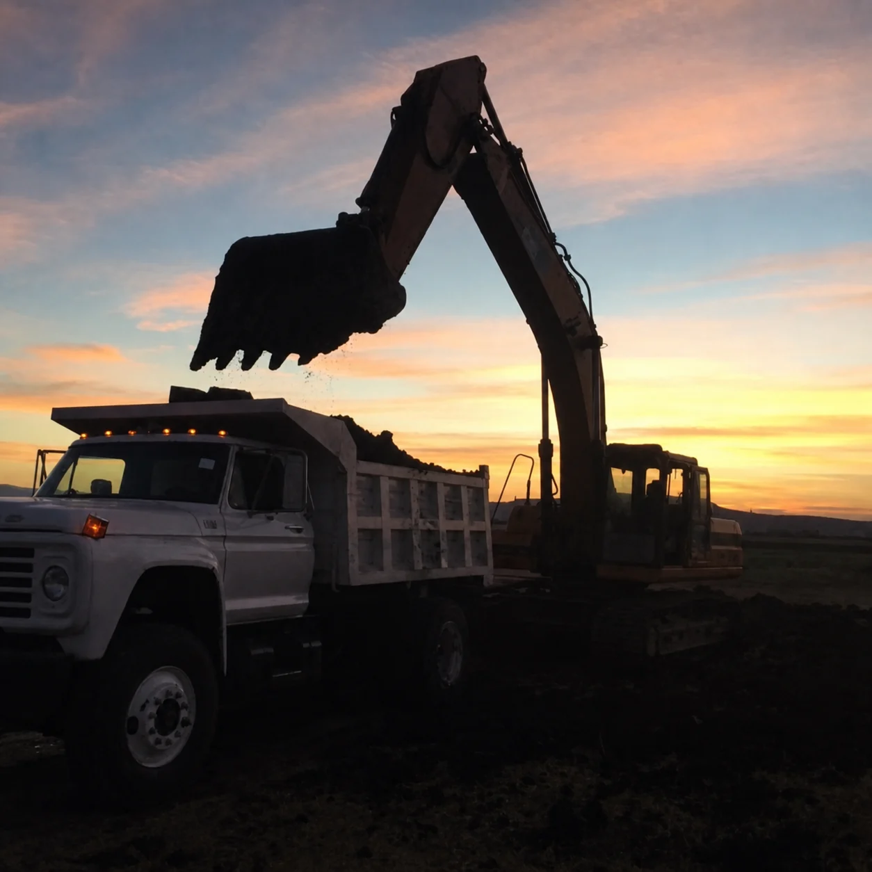 Excavadora cargando material en un camión de CUMICSA al atardecer